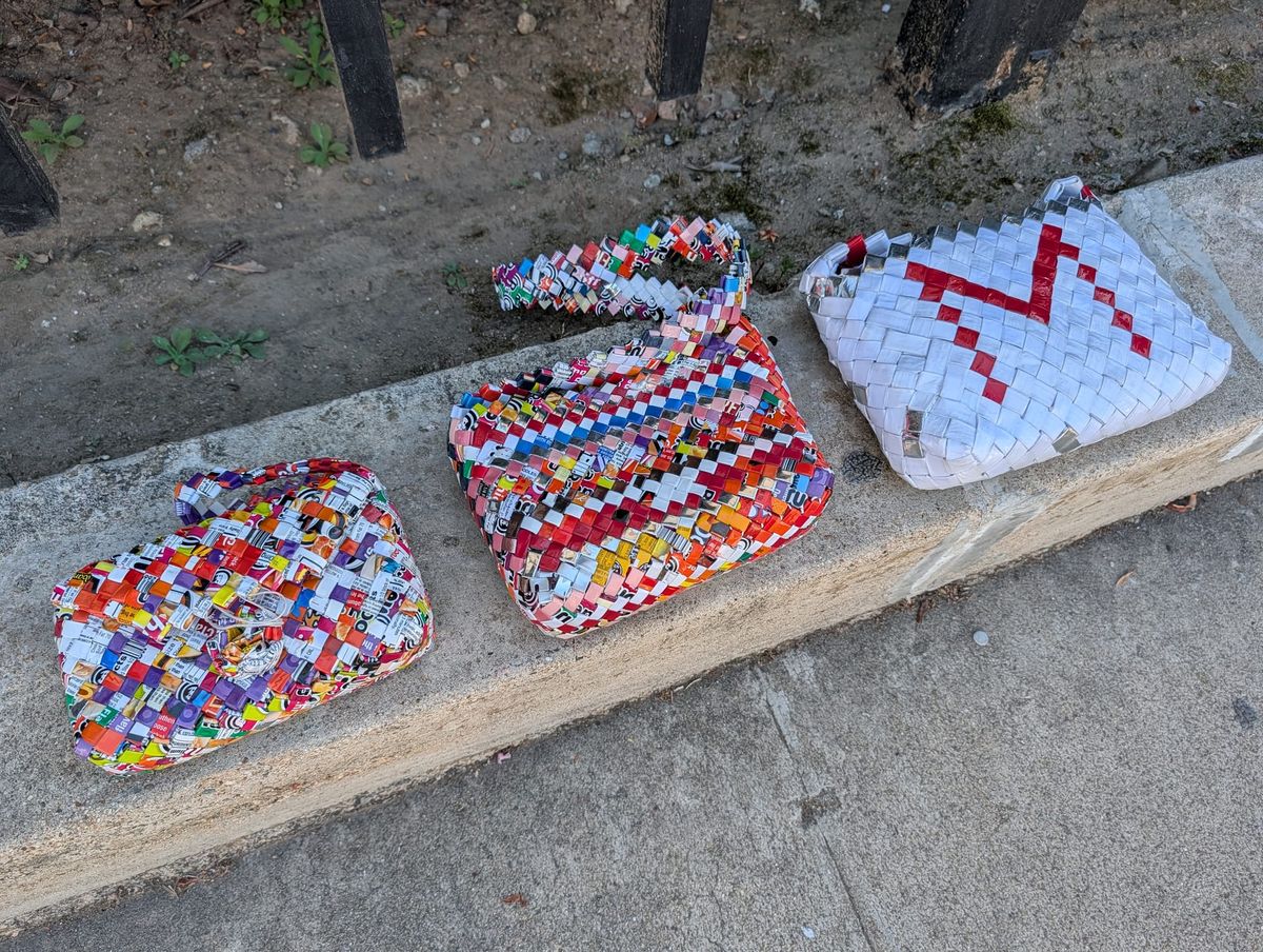 Three woven purses in several colors on a gray sidewalk