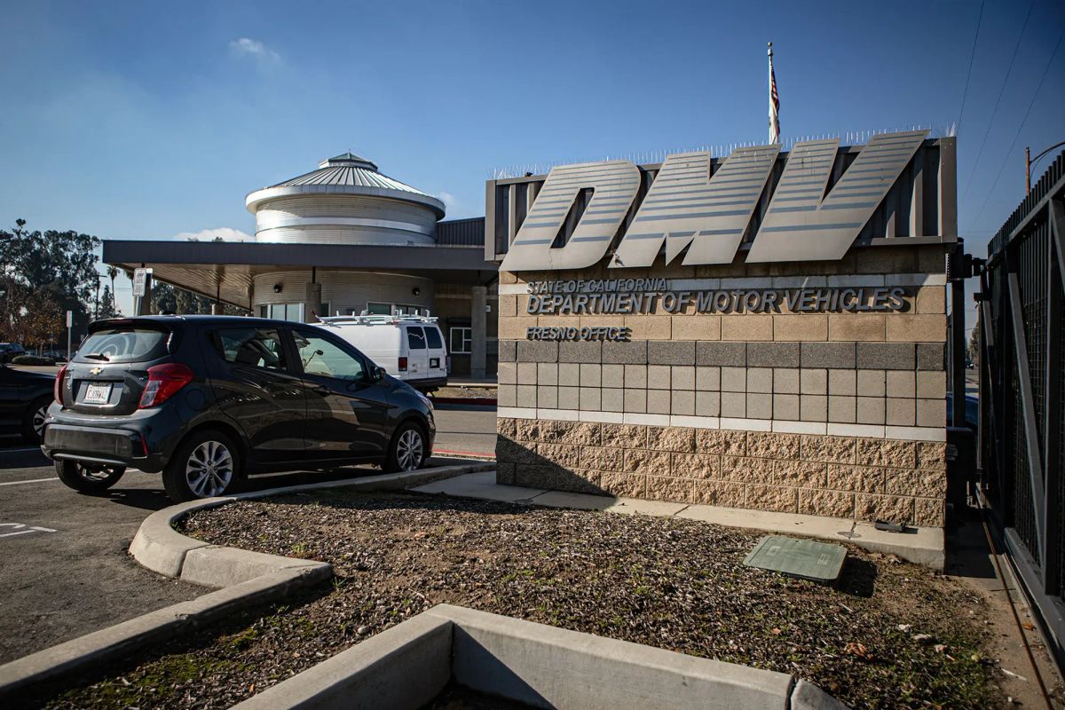 A concrete sign that says DMV with a small compact car parked next t