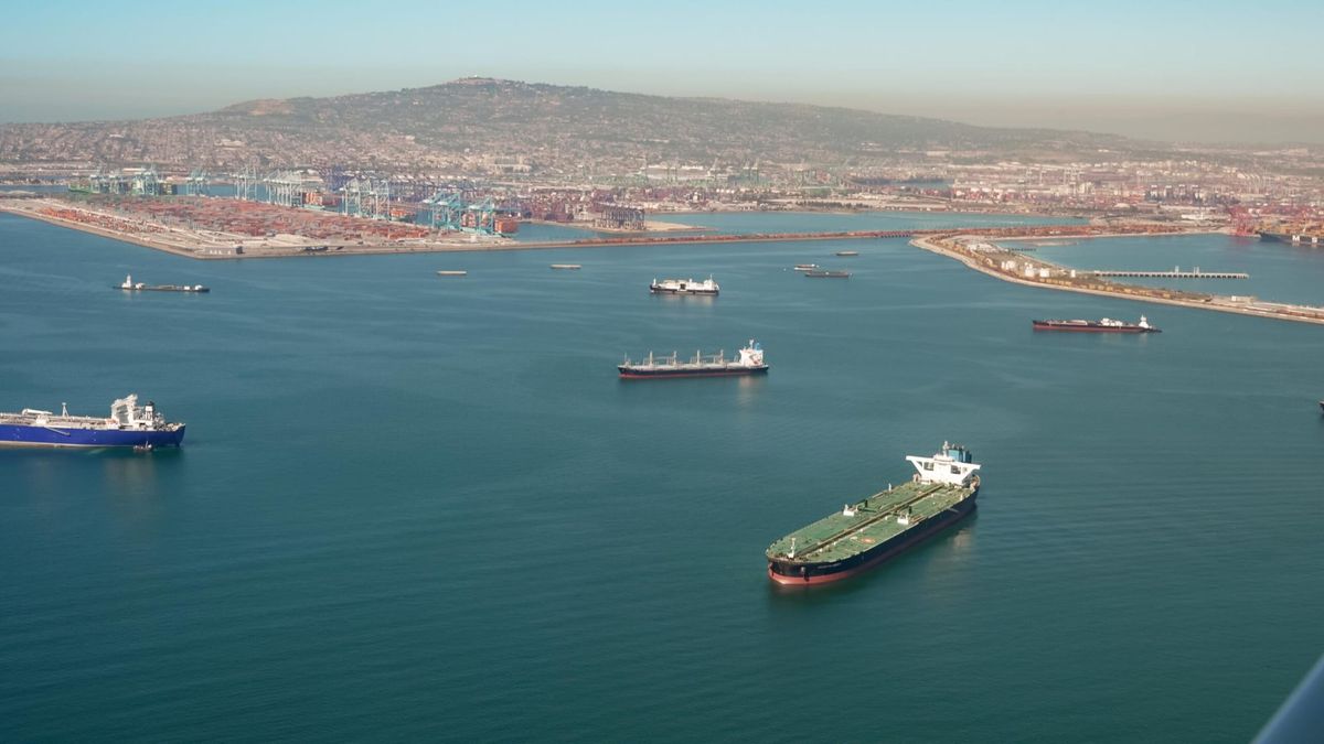 Picture of oil tankers floating in the water in front of a port with a mountain in the background