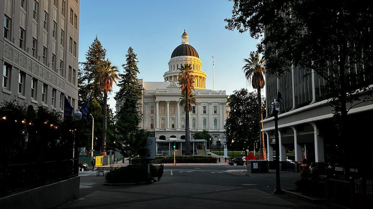 Picture of a state capitol building framed between two buildings with palm trees in front of it.