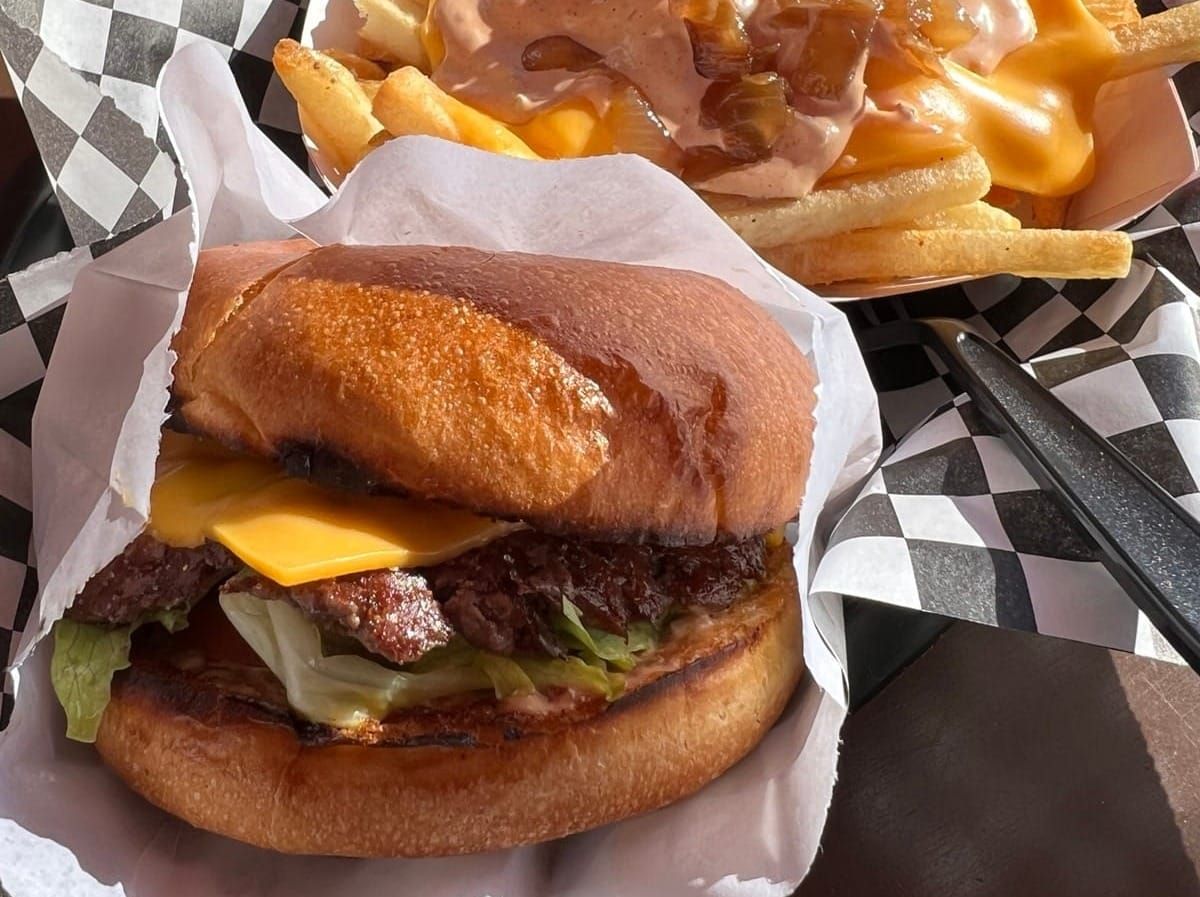 A burger wrapped in paper with a carton of fries drizzled in cheese and topped with meat