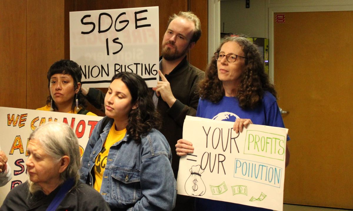 A group of demonstrators hold signs reading "SDGE is union busting" and 'Your Profits = Our Pollution"