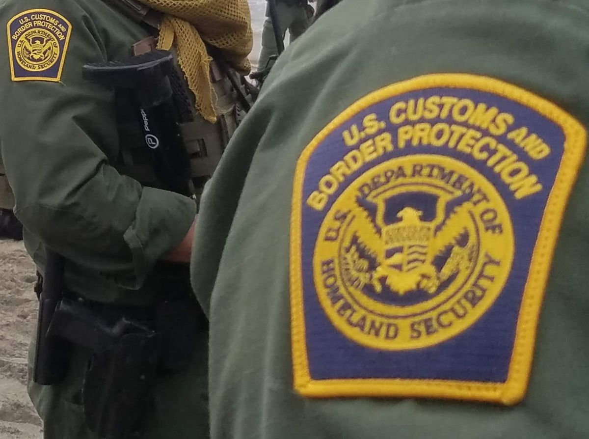 a close up of the Customs and Border Protection logo patch on a green uniform with another person in the same uniform standing behind