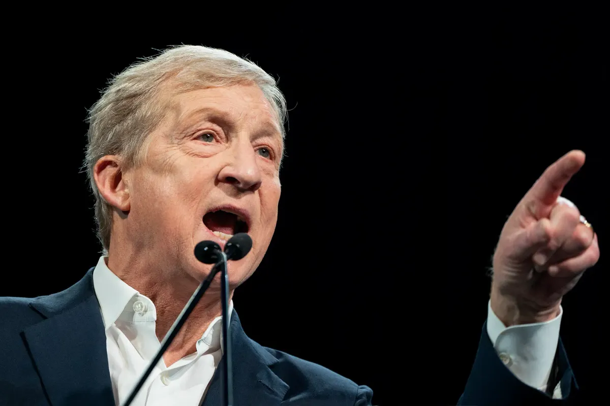 A man in a blue suit points his finger while standing in front of a microphone
