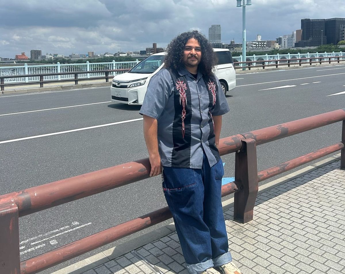 A person with curly hair stands in front of a street 