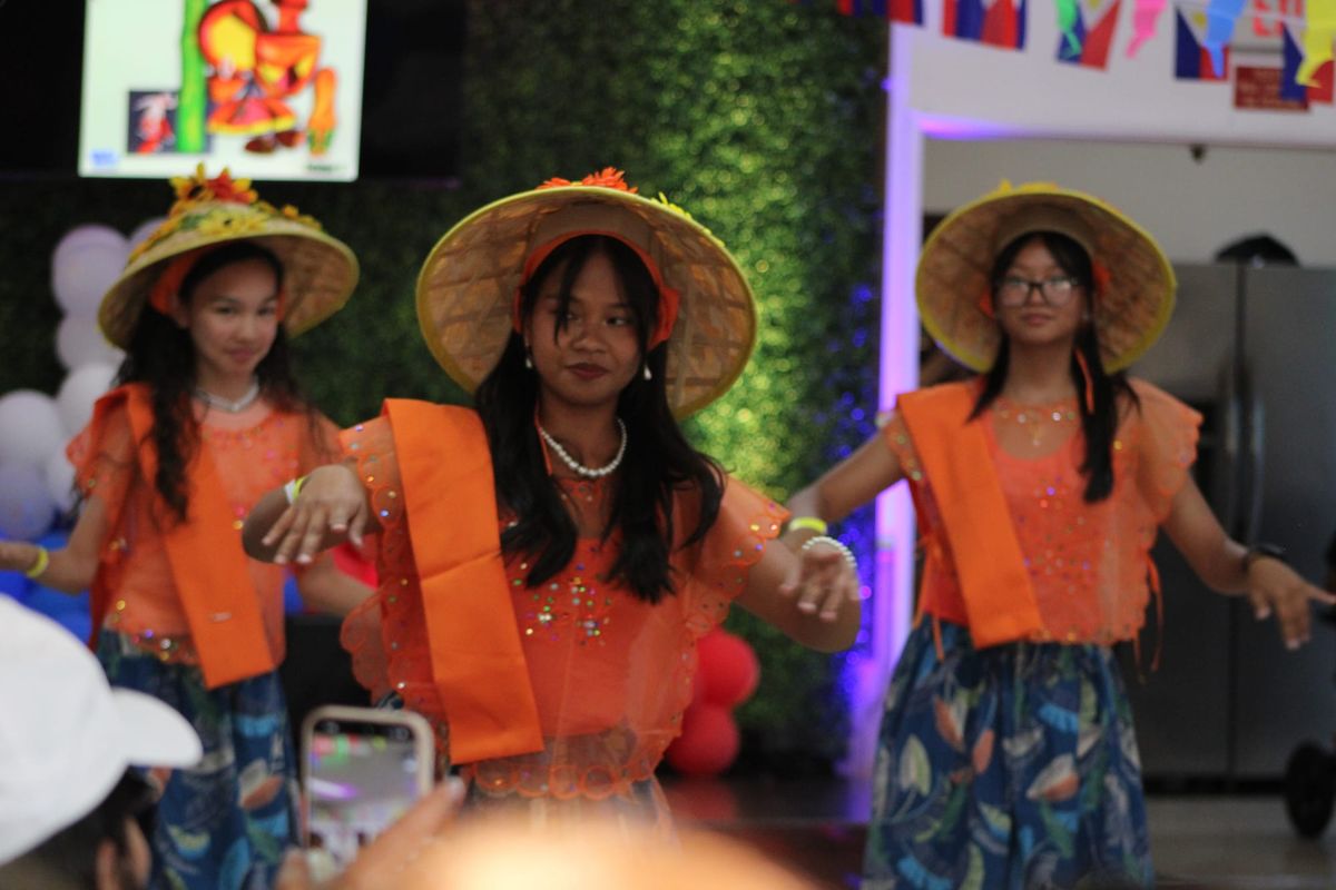 Three people dance in orange tops and straw hats 