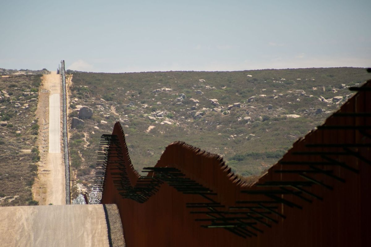 A rust red wall cuts a line through a scrubby desert landscape