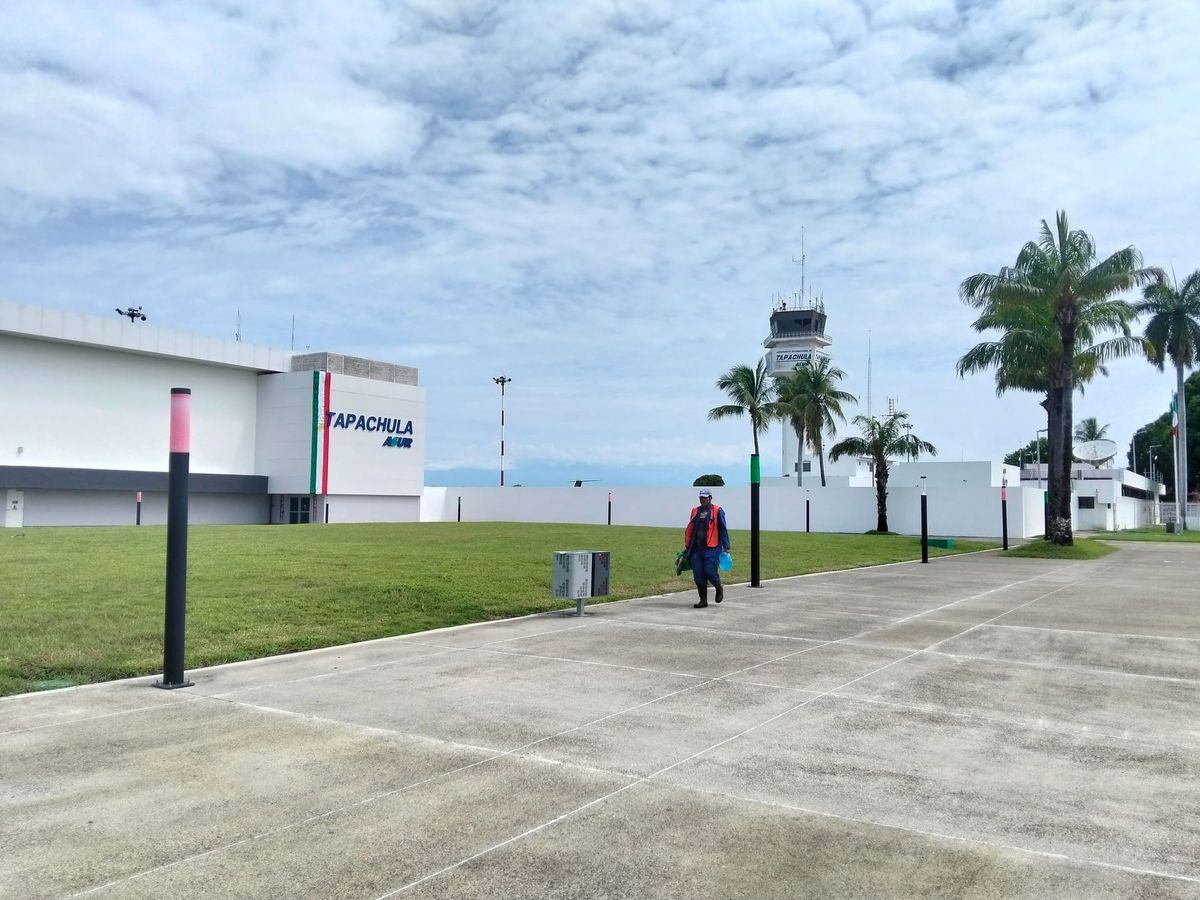A worker in an orange vest walks on a sidewalk in front of a control tower