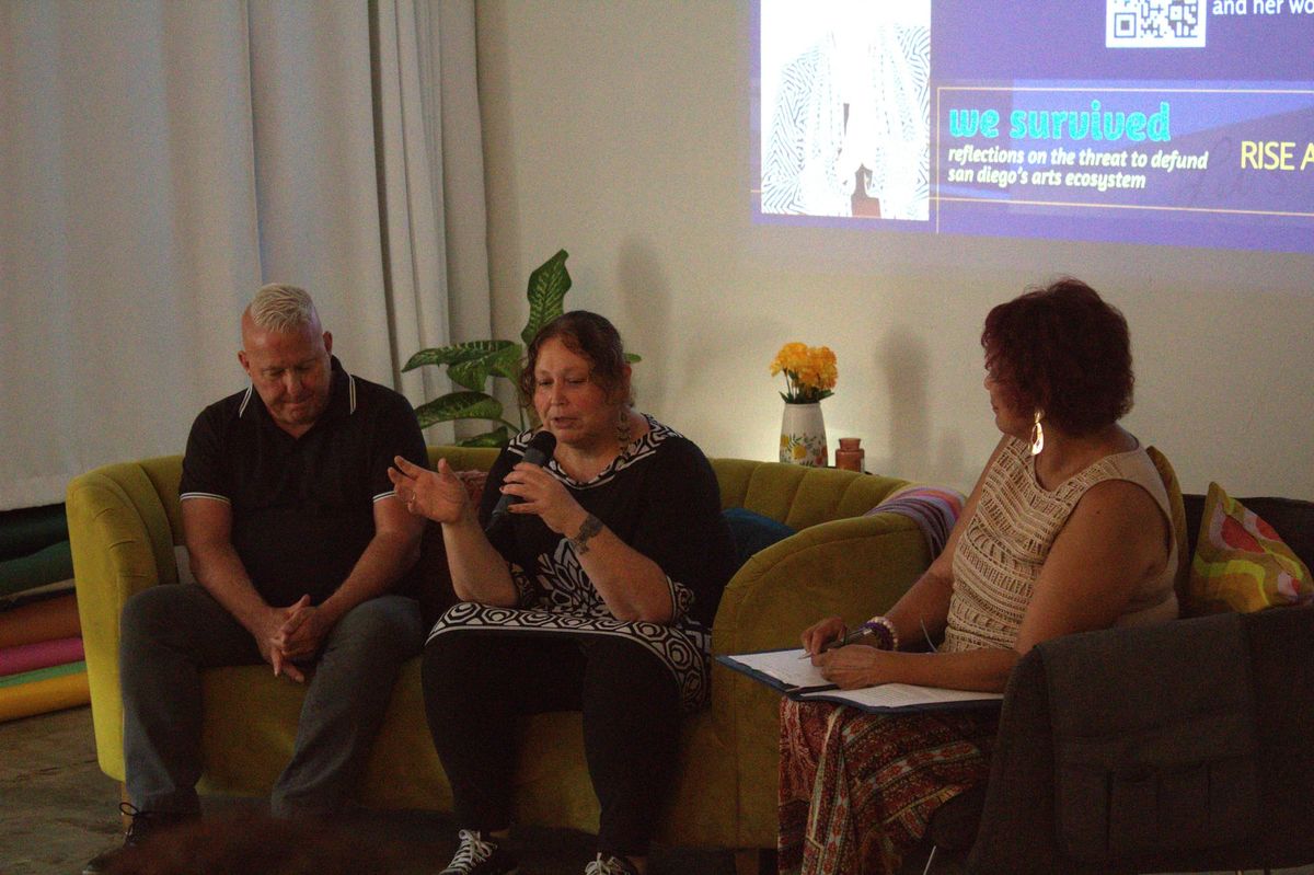 A man and woman speaker sit on a couch talking while facing attendees. 