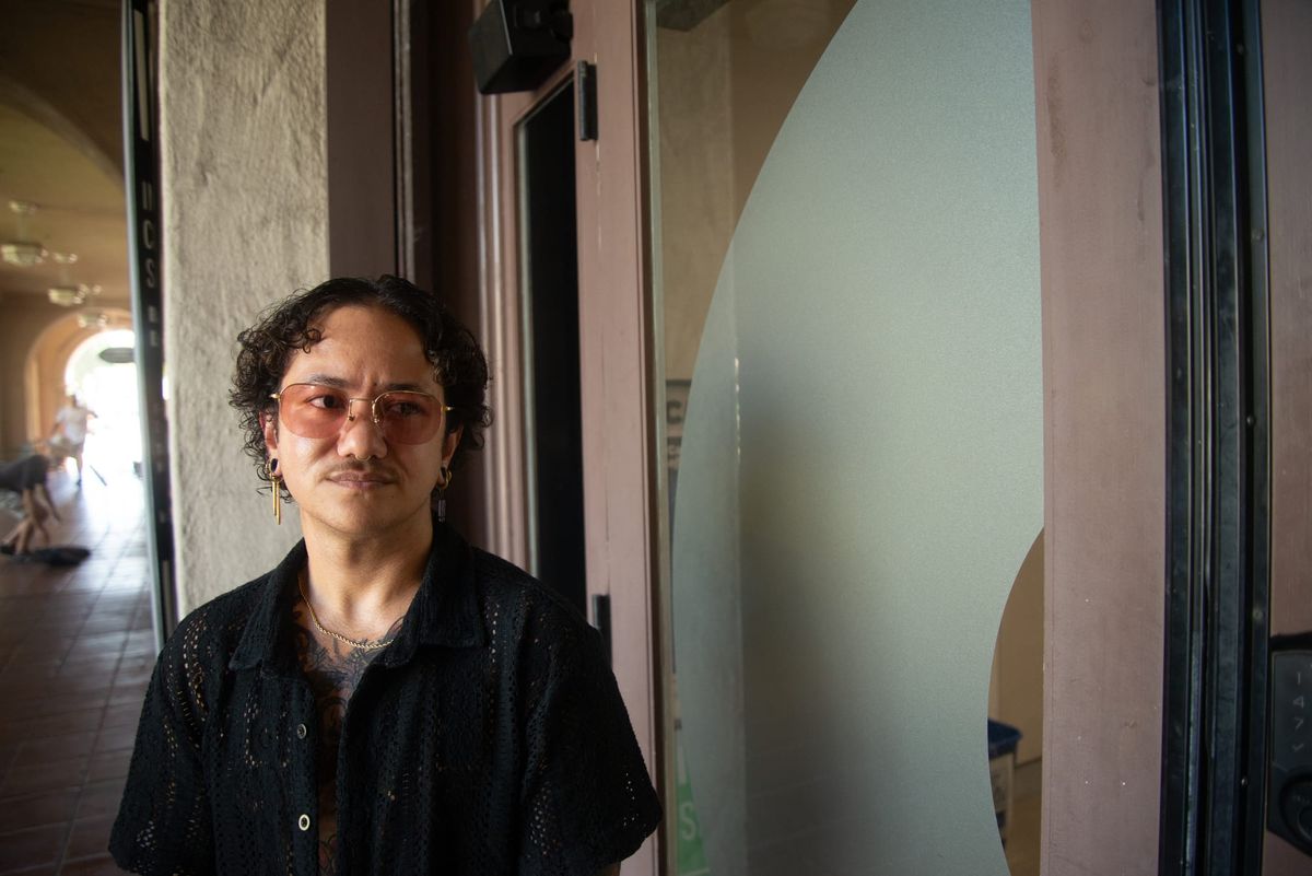 A person with sunglasses and a black shirt stands in front of a glass door