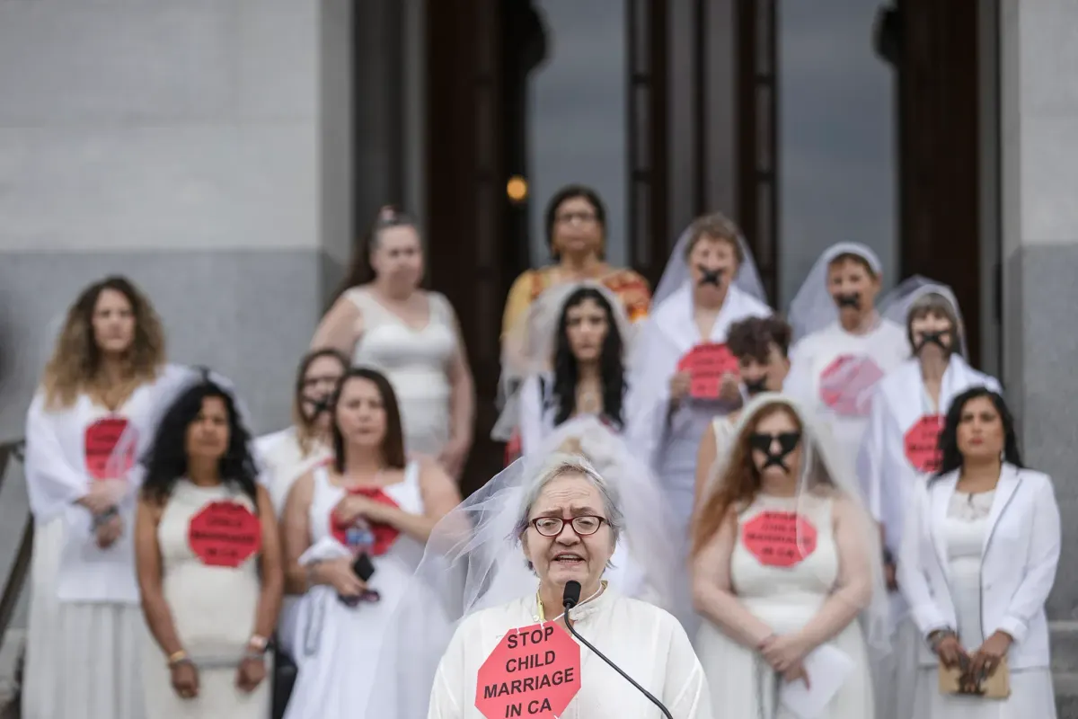 A woman in a veil and wearing white holds a sign that says "stop child marriage in CA"