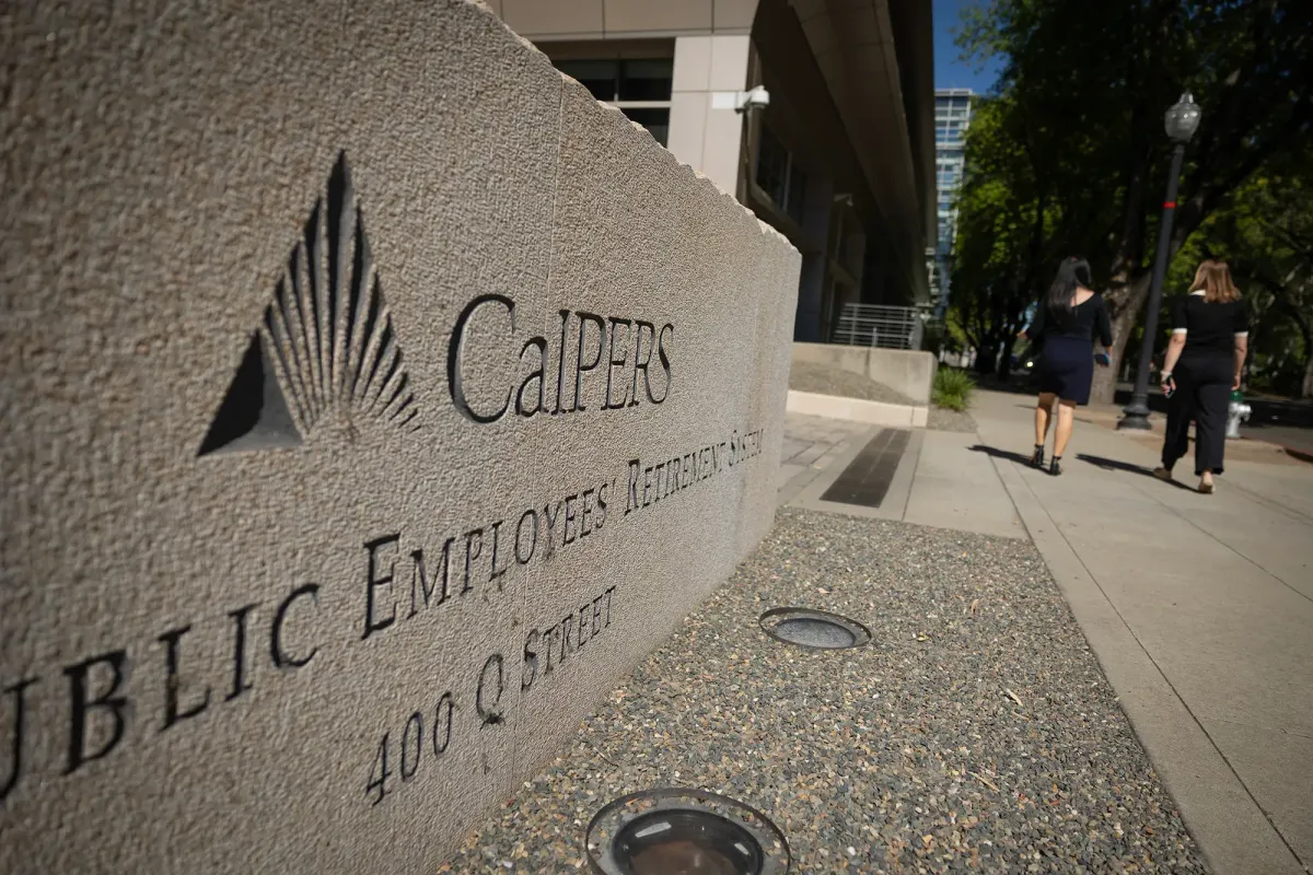 Concrete sign that says CalPERS with people wearing black walking away from the camera next to it