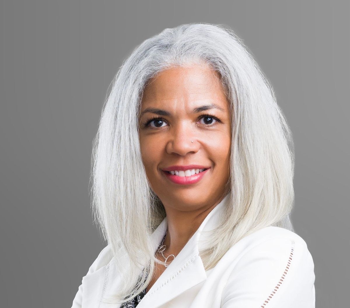 Picture of a woman smiling wearing a white blazer in front of a gray background