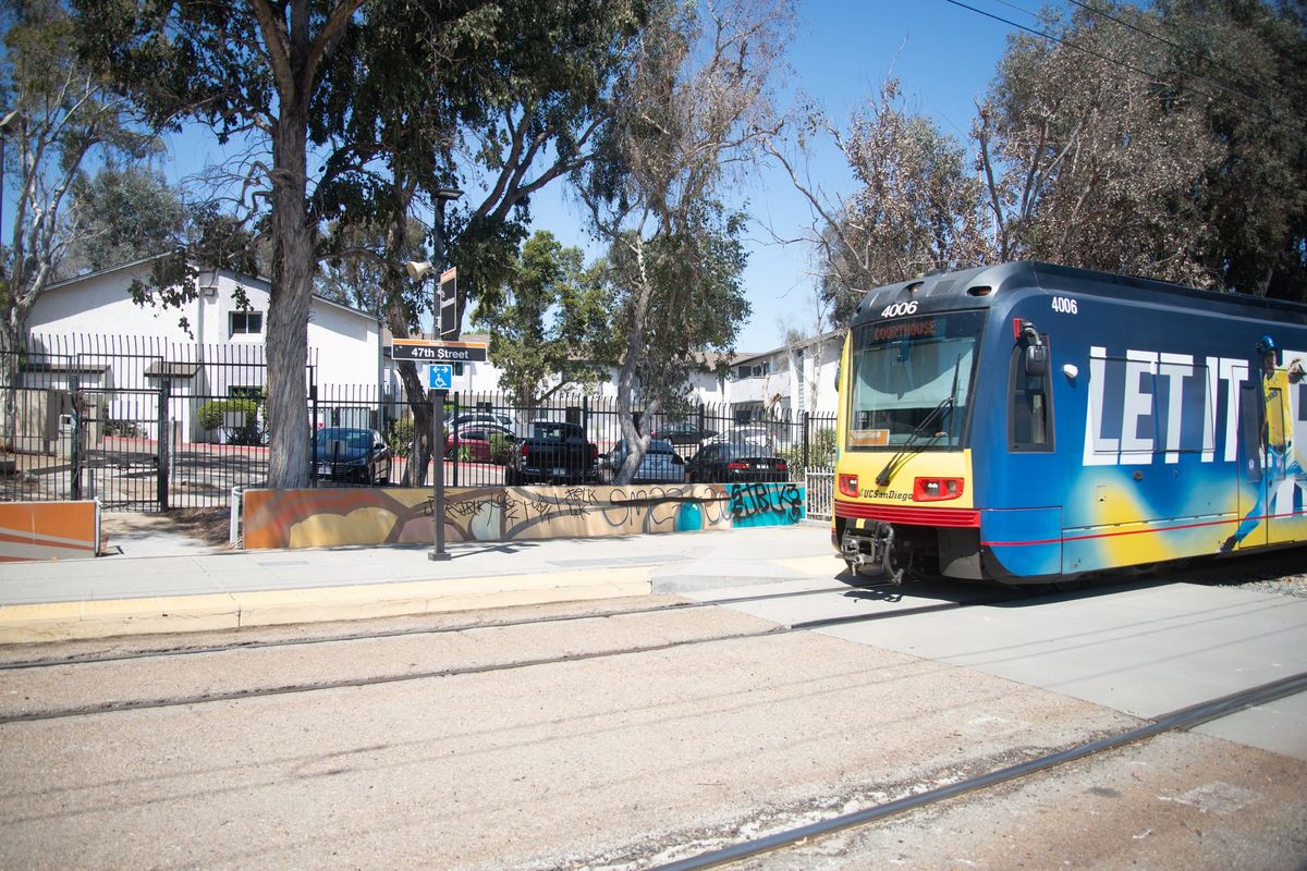 A sign says To El Cajon with another underneath that says 47th Street next to two rows of trolley tracks and a trolley