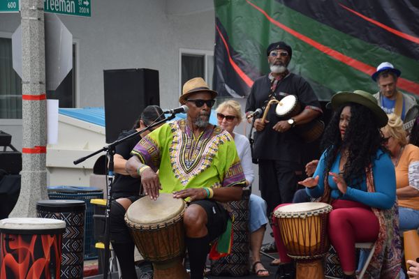 a group sits on the stage of an outdoor event performing with african drums