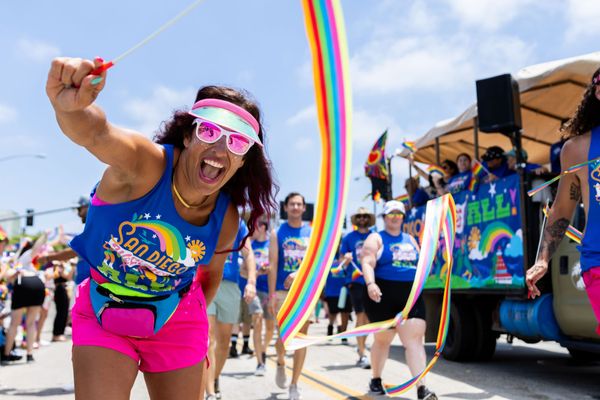 A person wearing bright clothes and a visor waves a rainbow ribbon