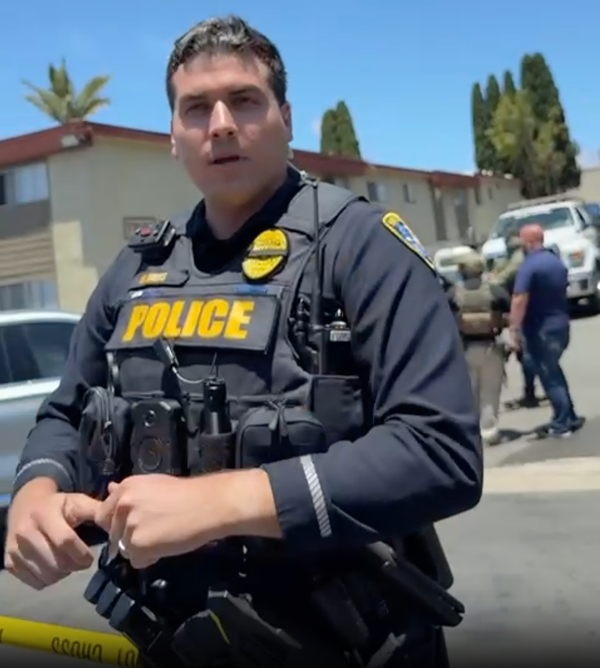 A police officer speaks in front of ICE agents at an apartment complex