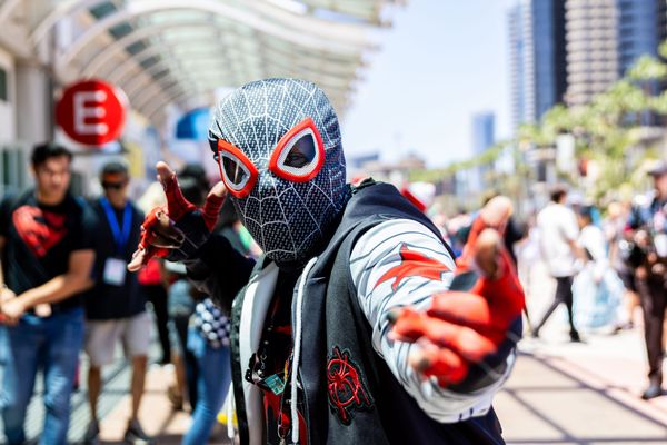 A man in a spider-man costume poses outside a convention center with people walking behind him