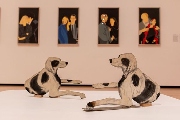 Two 2D painted dog statues are on display in front of paintings in a museum 