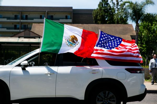 Mexican and American flags wave as a car drives by.