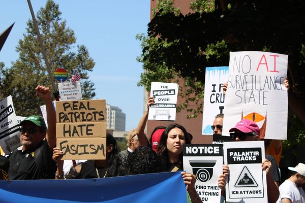 A group of demonstrators hold up letter signs will messages like “Real Patriots Hate Fascism" and ”No AI Surveillance State" outside