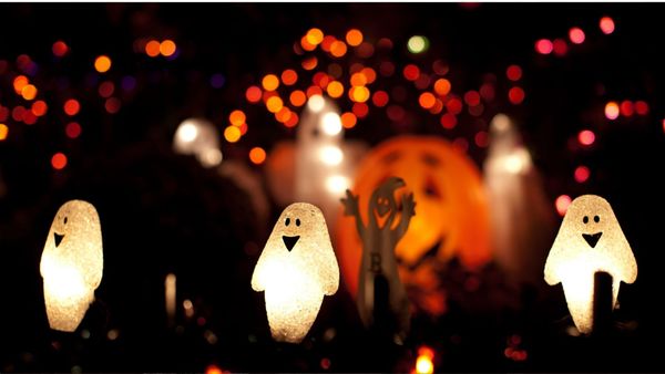 Halloween decorations of ghosts and a pumpkin lit up at night.