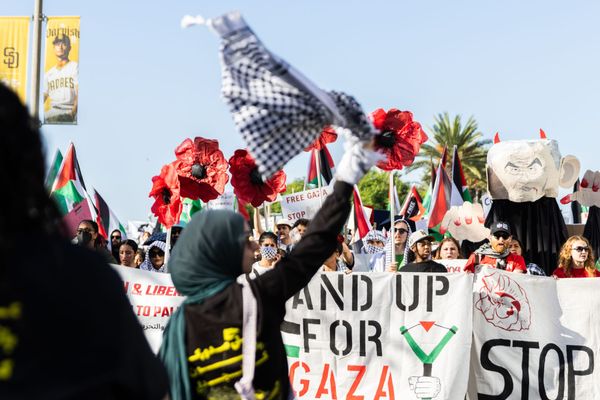 A woman waves a keffiyeh in front of a group of people marching and holding signs that read "stand up for gaza."