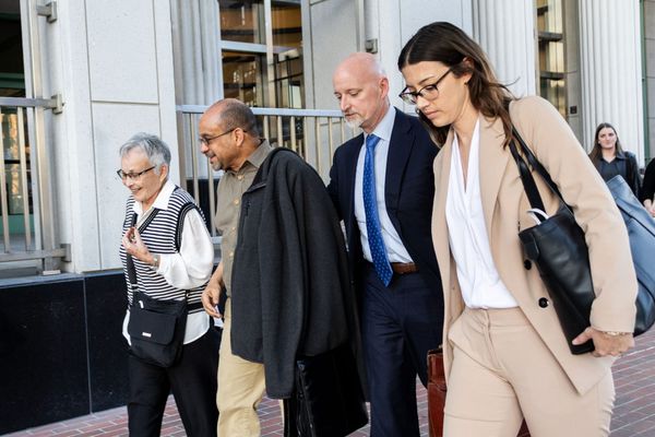 Two men and two women walk toward the left side of the frame with a building close behind them.