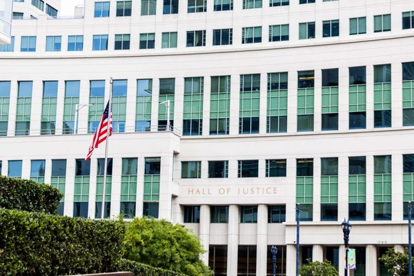 Picture of a building that says "Hall of Justice" with a bush in front of it.