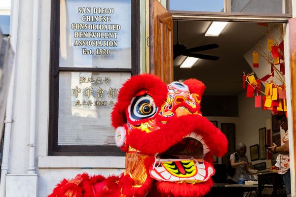 A red lion dancer stands in front of a window and open door of an organization's building.