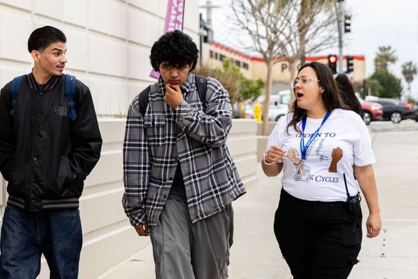 A women and two teens walk down the street talking.