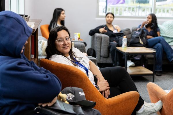 A woman sits with teenagers on chairs and sofas talking.