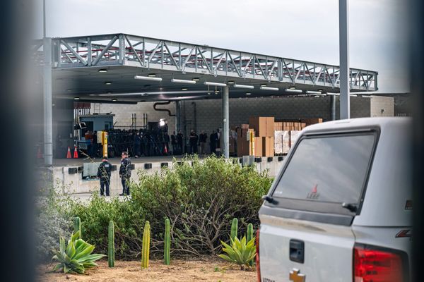 Fence posts frame a truck and a building where people gather underneath by some boxes