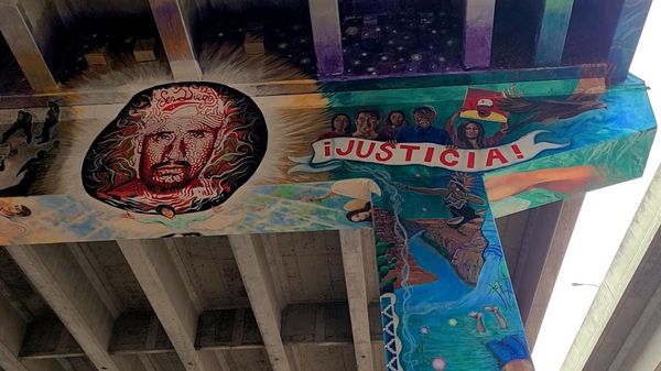A man's face and the word justicia are painted on concrete pillars underneath a highway bridge