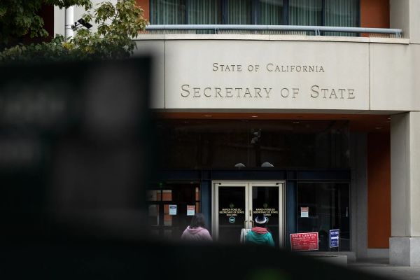 A concrete building with a sign that says State of California Secretary of State with two people walking into the glass doors
