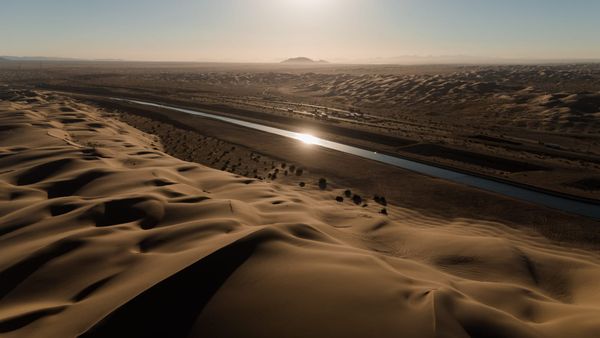 A thin strip of water runs through sand dunes that stretch into the distance