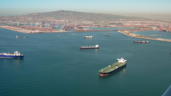Picture of oil tankers floating in the water in front of a port with a mountain in the background