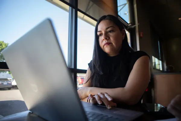 A woman in a black shirt sits in front of a laptop computer next to a large window