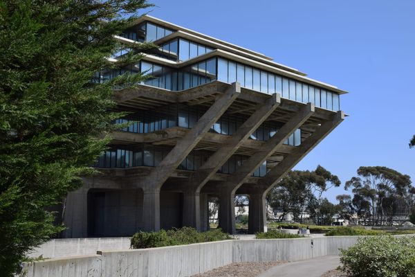 Picture of the outside of a brutalist-style college library with trees on the left and in the background