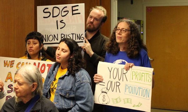 A group of demonstrators hold signs reading "SDGE is union busting" and 'Your Profits = Our Pollution"