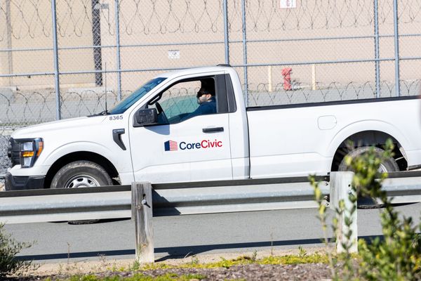 A white trick with the logo CoreCivic drives next to a fence with concertina wire