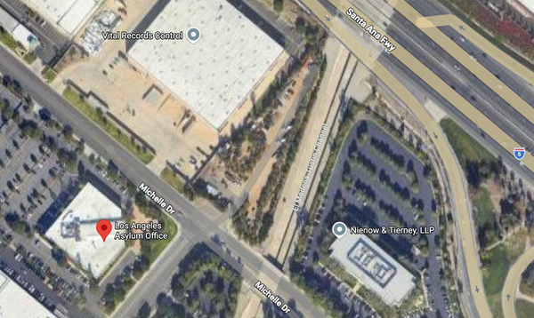 A satellite view of a building with a large parking lot next to a much bigger building and a highway