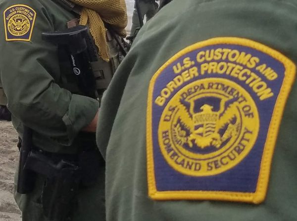 a close up of the Customs and Border Protection logo patch on a green uniform with another person in the same uniform standing behind