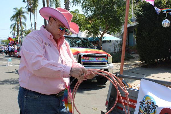 A person in a pink button down and pink cowgirl hat holds a pink lasso in front of a rainbow truck that says love is love