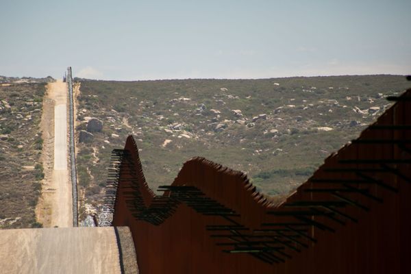 A rust red wall cuts a line through a scrubby desert landscape