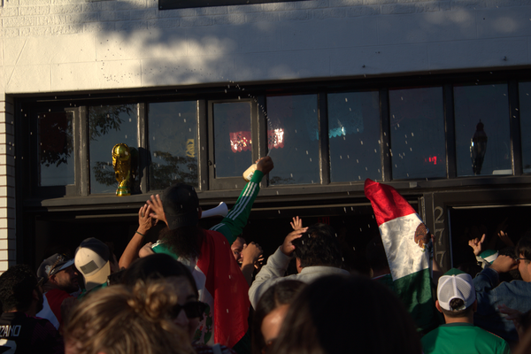 A FIFA World Cup trophy sits on the ledge of a restaurant’s windows as fans below celebrate by putting up a flag and spraying beer. 