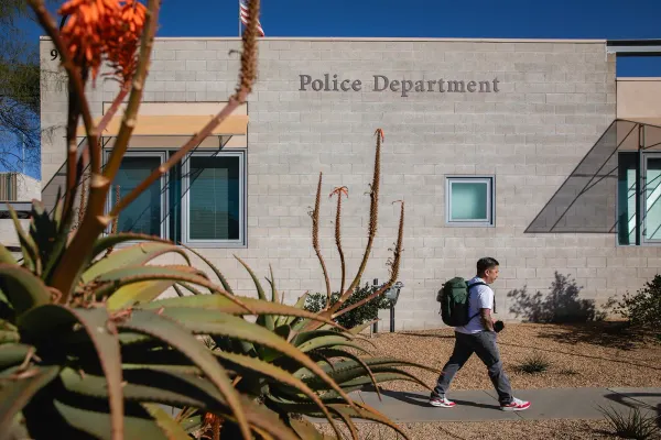 A plant in the foreground and a person walking next to a beige building that says Police Department