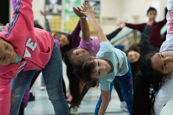 Children stretch their arms high as they lean sideways down toward their feet