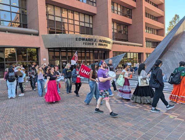 A person in a purple shirt banging on a drum walked with a group of people around a brick plaza