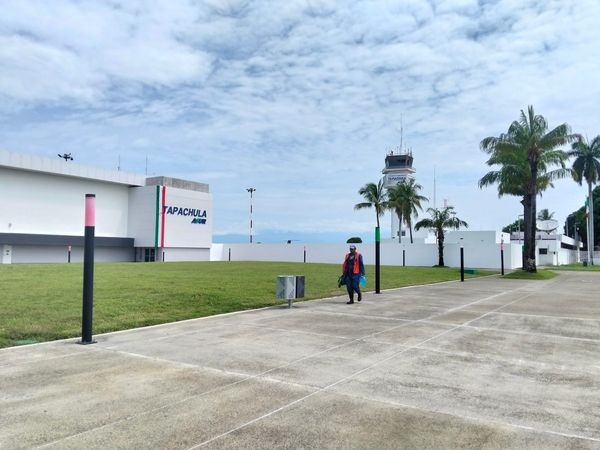 A worker in an orange vest walks on a sidewalk in front of a control tower